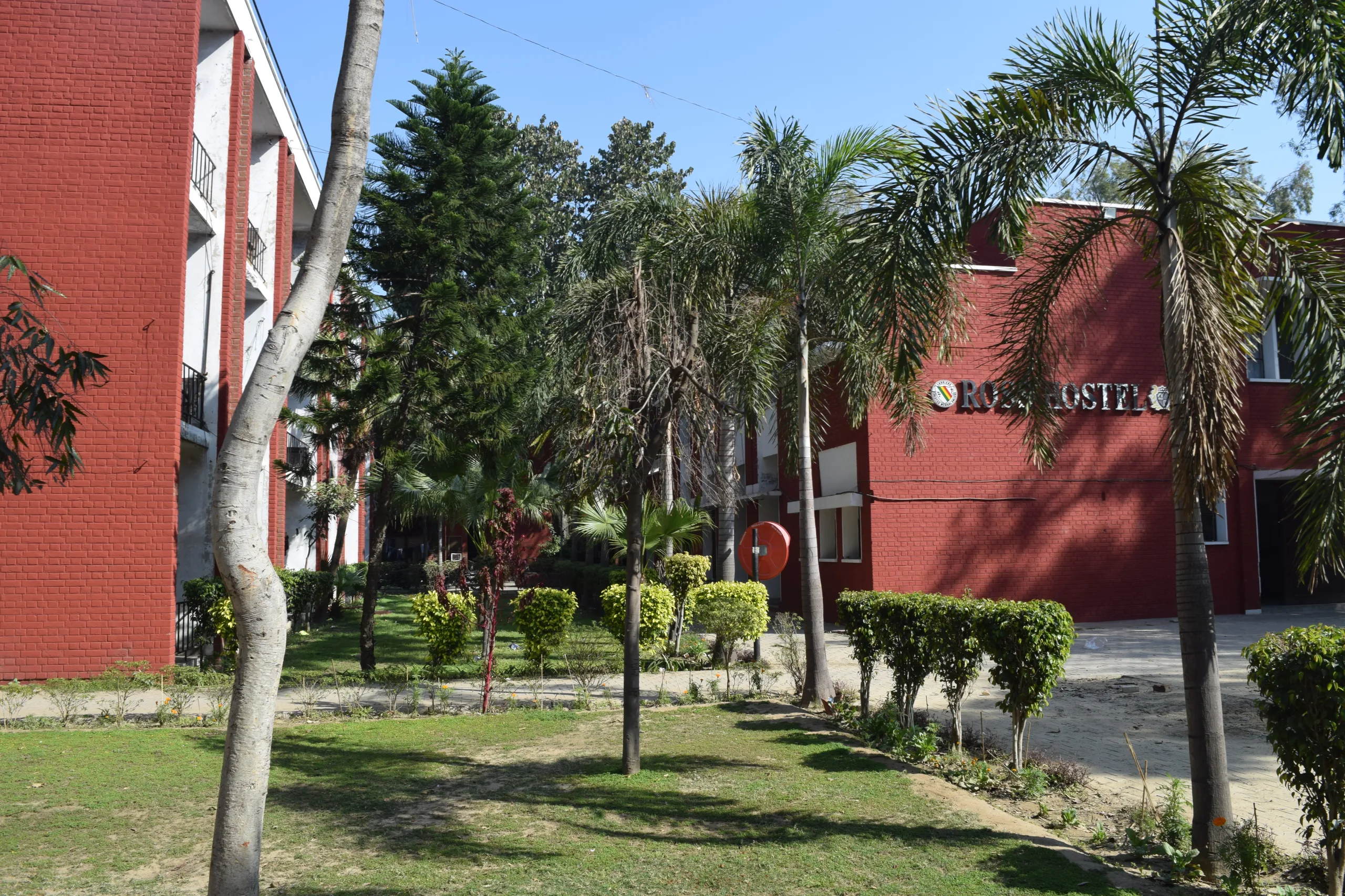 Red-brick campus buildings surrounded by green lawns, trees, and shrubs on a sunny day; the sign Research is partially visible on one building.