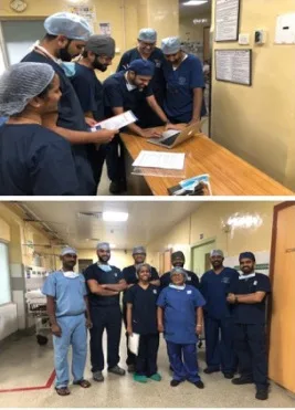Group of doctors in surgical scrubs reviewing notes around a desk in a hospital setting.