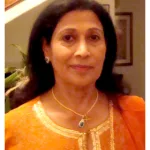 Portrait of Dr. Elizabeth Paul, wearing an orange traditional outfit with gold embroidery and a cross pendant necklace, offering greetings as Alumni President of Ludhiana Christian Medical College.