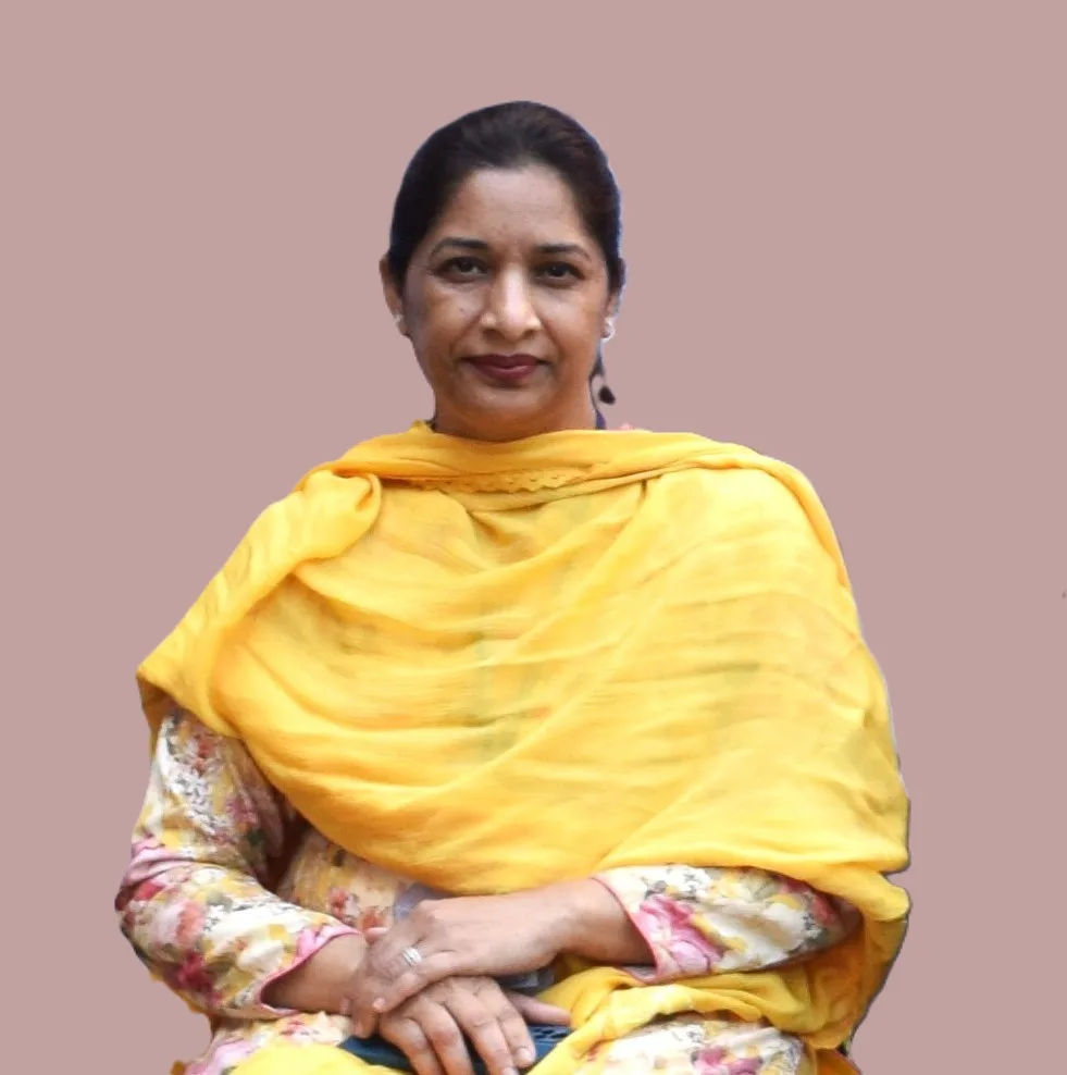 A woman with dark hair tied back, wearing a yellow shawl over a floral top, sits with her hands folded on her lap against a plain light brown background, reminiscent of portraits seen at the Christian Medical College in Ludhiana.